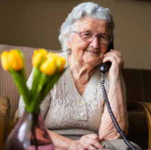afbeelding oudere dame aan de telefoon met bosje bloemen