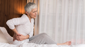 Stressed mature woman touching her painful back and feeling discomfort in her bedroom, Back pain concept